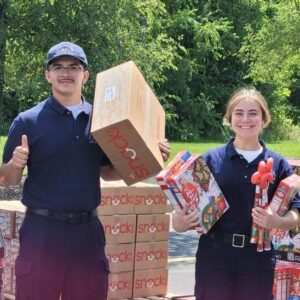 Photo of two youth holding snack boxes and cereal boxes. There is a pallet of food behind them and they are smiling for the camera.