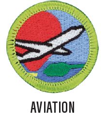 Image of a Aviation merit badge. The badge is blue with a green border with a plane taking off, a hot air balloon in the background.