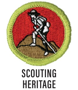 Image of the Scouting Heritage merit badge. The badge is red with a green border with a scout walking a trail with a walking stick and hiking pack