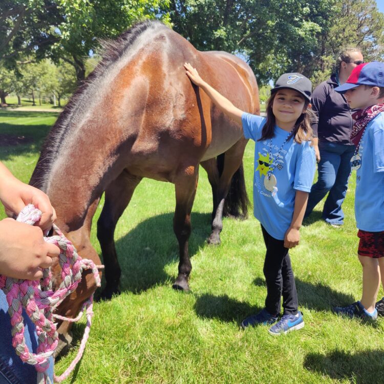 Photo of several youth standing outside next to a horse. One youth is petting the horse and smiling.