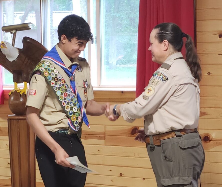 Photo of two scouts, one youth and an adult. The youth is dressed in Eagle regalia. They are shaking hands.